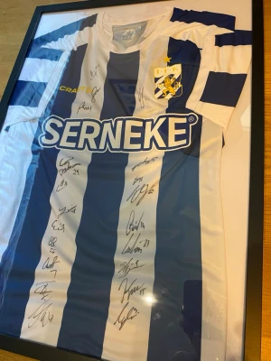 IFK Göteborg matchtröja signerad - Säljer en blåvit randig IFK Göteborg matchtröja från Craft med klubbmärke och sponsorlogga SERNEKE på bröstet. Tröjan är signerad av flera spelare och har klassisk rund hals och korta ärmar. Perfekt för dig som älskar fotboll och samlar på supporterprylar. 2024-2025 IFK’s trupp, oanvänd. Skickas utan ram.