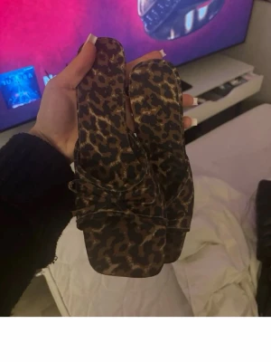 Leopardmönstrade sandaler med klack - Säljer ett par trendiga sandaler med leopardmönster och låg klack. De har fyrkantig tå och breda remmar över foten. Perfekta för dig som vill sticka ut med ett djurmönster. Materialet ser ut att vara syntet eller tyg.
