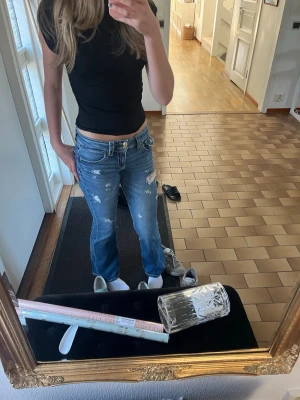 Blå slitna bootcut jeans - Säljer ett par blå bootcut jeans med slitningar och hål för en trendig look. Jeansen har låg midja, fem fickor och dubbla knappar i midjan. Pris kan diskuteras, från Gina Tricot i strl 164. Slitningarna har jag gjort själv så säljs ej på deras hemsida. 