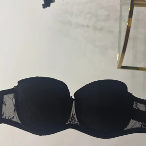 Svart push-up bh med spetsdetaljer - Snygg svart push-up bh med vadderade kupor och fina spetsdetaljer på sidorna. Bh:n har justerbara axelband och klassisk hysk- och hakknäppning bak. Perfekt för dig som vill ha extra stöd och en elegant look.