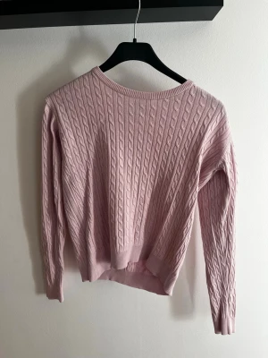 Ljusrosa kabelstickad tröja - Säljer en ljusrosa kabelstickad tröja från c'est la vie. Tröjan har rund halsringning, långa ärmar och ribbade muddar vid ärmslut och nederkant. Perfekt för dig som gillar en klassisk och söt look med mjukt material.