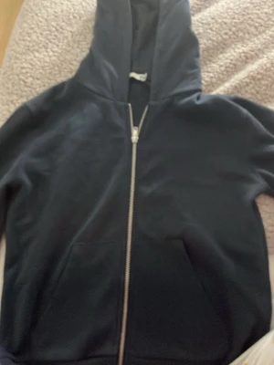 Mörkblå zip hoodie från 157 - Klassisk mörkblå  hoodie från 157 med dragkedja framtill och stor huva. Hoodien har två fickor på magen och är gjord i mjukt, bekvämt material. Perfekt för chill dagar eller när du vill ha en enkel och stilren look.