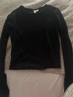 Svart långärmad topp från Divided - En enkel och stilren svart långärmad topp från Divided. Toppen har en rund halsringning och är croppad i modellen. Perfekt att matcha med höga jeans eller kjol för en clean look.