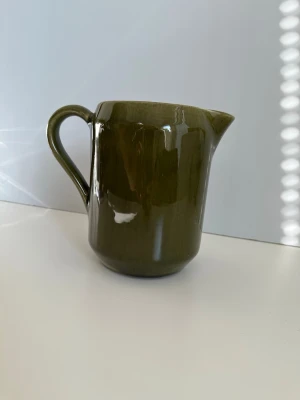 DECO Grön keramik kanna med handtag - Vacker stilren kanna från anrika svenska stengodstillverkaren DECO Helsingborg i mörkgrön / mossgrön keramik med blank finish. Kannan har ett rejält handtag och en bred pip som gör det enkelt att hälla. 17cm hög. Fint skick!
