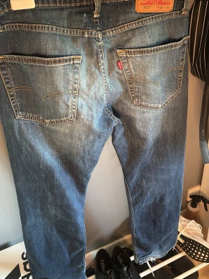 Levi's 527 blå jeans slim bootcut fit - Säljer ett par klassiska blå Levi's 527 jeans med rak passform och fem fickor. Jeansen har snygga slitningar och kontrastsömmar, samt den ikoniska röda Levi's-lappen på bakfickan. Tillverkade i slitstark denim, perfekta för en avslappnad stil.