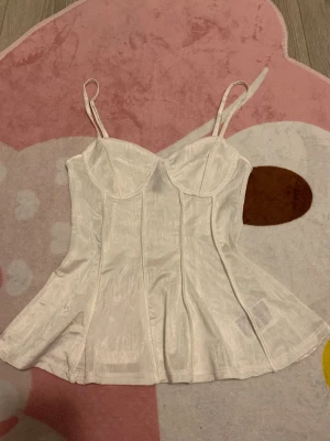 Vit volang topp - Söt vit korsettliknande topp från H&M Divided i storlek XS! Ganska så tunn med volang nertill. Den är väldigt liten i bysten så den kommer inte passa någon med en större byst! (⚠️jag tar ENDAST instabox)
