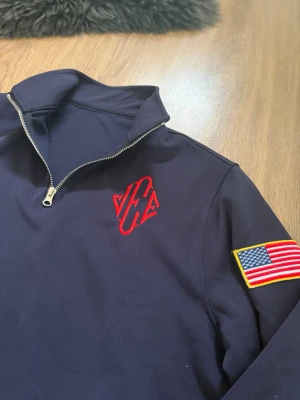 Epstein tröja  - Mörkblå långärmad tröja med halv dragkedja och ståkrage. Röd brodyr på bröstet och amerikansk flagga på ärmen. Perfekt för en sportig och stilren look. Snygg nostalgisk tröja i storlek M.                      Skriv om ni har några funderingar!😃