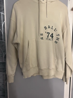 Beige hoodie med tryck och luva - Säljer en beige hoodie med stor luva och känguruficka framtill. Tryck med text och siffror i mörkgrönt på bröstet och stora bokstäver längs ena ärmen. Skön oversized passform och ribbade muddar vid ärmslut och nederkant. Perfekt för en chill och avslappnad stil. Kostar 1800 ny pris💕 aldrig använt och pris går att diskutera💕