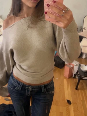 Beige offshoulder stickad tröja Gina Tricot - Trendig beige stickad tröja från Gina Tricot i offshoulder-modell. Tröjan har lång ärm, ribbad struktur och en croppad passform som ger en snygg siluett. Perfekt att matcha med jeans eller kjol för en cool look.