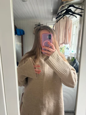Beige oversized stickad tröja - Säljer en beige oversized stickad tröja med breda ribbade muddar vid ärmslut och nederkant. Tröjan har en avslappnad passform och är gjord i ett mjukt material, perfekt för lager på lager. Passar dig som gillar en chill och enkel stil.