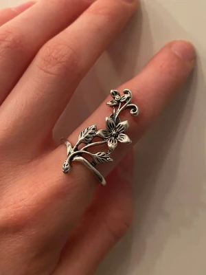 Silvrig ring med blommor och blad - Unik silvrig ring i metall med detaljerade blommor och blad som slingrar sig runt fingret. Ringen har en öppen design och fina snirkliga former som ger en bohemisk och romantisk känsla. Helt oanvänd och ej äkta silver 🫶
