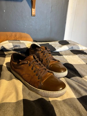 Bruna låga sneakers i mocka och läder - Snygga bruna sneakers med ovandel i mocka och tåparti i blankt läder. Vill bara bli av med pga att dem inte passar mig längre. Stl 10 (44-45). Dustbag ingår, fraktar samma dag som de köps✅