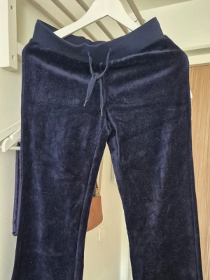 Mörkblå velourbyxor med dragsko - Mörkblå byxor i mjuk velour med bred resår och dragsko i midjan. Raka ben och två bakfickor med lock ger en chill vibe. Perfekta för avslappnade dagar när du vill vara både bekväm och snygg.        Centilong storlek 158/ 164. Nya inte använda