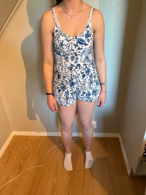 Vit och blå blommig jumpsuit - Vit blommig jumpsuit med blåa blommor på. Den har lätt tyg så den är bra till varma sommardagar. Den är från H&M