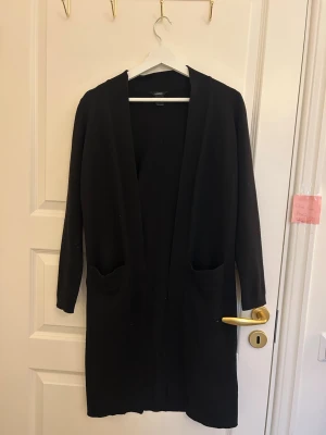 Svart lång kofta från Lindex - Säljer en svart lång kofta från Lindex i storlek XS. Koftan har öppen front, två fickor framtill och långa ärmar. Perfekt att slänga över en t-shirt eller topp för en enkel och clean look.