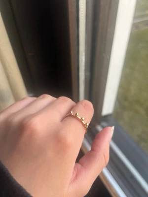 Tunn guldfärgad ring med pärldetaljer - En stilren och tunn ring i guldfärg med små pärlliknande detaljer längs ovansidan. Ringen har en minimalistisk design som passar perfekt för dig som gillar enkla men unika accessoarer. Materialet ser ut att vara metall med en blank finish.