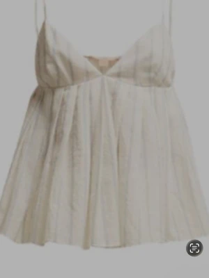 Ljusrandig linnetopp med tunna band - Söt ljus linnetopp med tunna axelband och subtila vertikala ränder. Toppen har v-ringning och ett luftigt, flödande fall som ger en avslappnad och somrig känsla. Perfekt för varma dagar och enkel att styla med jeans eller kjol.