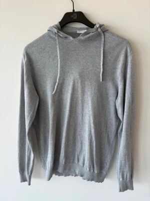 Ljusgrå hoodie i bomull och kashmir - Mjuk och stilren ljusgrå hoodie med huva och dragsko. Tillverkad i en lyxig blandning av bomull, siden och kashmir som ger en skön och exklusiv känsla. Perfekt för dig som gillar en enkel men snygg look. Långa ärmar och ribbade muddar.