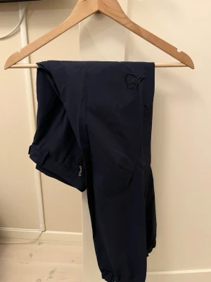 Mörkblå byxor Norrøna - ett par mörkblå mjukisbyxor från Norrøna med resår i benslut och dragkedja vid fickan. Byxorna har en avslappnad passform och är perfekta för chill dagar. Snygg logga på benet och mjukt material.