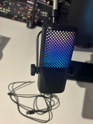 Svart USB-mikrofon med RGB-belysning Xbox - Säljer en svart mikrofon med RGB-belysning som lyser i flera färger. Mikrofonen har ett metallgaller framtill och monteras på ett justerbart stativarm. USB-kabel för anslutning till dator ingår. Perfekt för streaming, gaming eller podd. Xbox