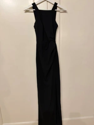 Svart lång klänning med breda axelband - Stilren svart långklänning med raka linjer och breda axelband. Klänningen har en figurnära passform och är gjord i ett slätt, vävt material som ger en elegant look. Perfekt för dig som gillar minimalistisk och tidlös stil. Klänningen är använd 1 gång och ordinarie pris är 800kr.