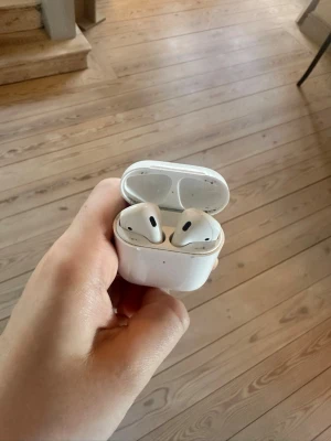 Apple AirPods med laddningsetui - Säljer ett par vita Apple AirPods med det klassiska laddningsetuiet. Trådlösa in-ear hörlurar i stilren design, perfekt för musik, poddar och samtal. Smidig magnetisk stängning på etuiet och enkel parkoppling med Apple-enheter.