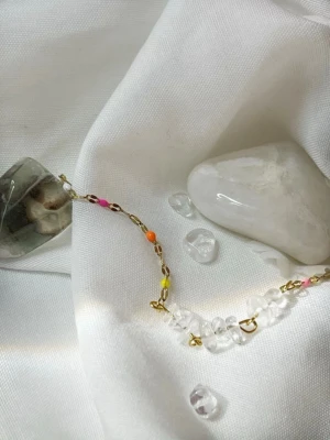 Fotlänk med bergskristall - Unikt Fotlänk med små färgglada pärlor i orange, rosa och gult, kombinerat med äkta Bergskristall  pärlor på en tunn guldfärgad kedja. Perfekt för dig som gillar detaljer och vill ha något som sticker ut. Materialet är stålfritt och nickelfria material.