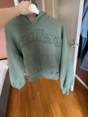 Grön Scuffers hoodie med broderad logga - Säljer en grön hoodie från Scuffers med stor broderad logga på bröstet och mindre logga på ryggen. Hoodien har huva, magficka och ribbade muddar vid ärmslut och nederkant. Använd fåtal gånger då den är lite för liten för mej !