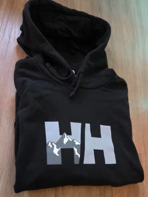 Svart hoodie från Helly Hansen - HH-tröja som har används ett få tal gånger men när den har används så har den varit varsamt använd, den har en ovanlig design som gör så att den står ut lite, skriv vid frågor. Priset är inte fast i sten.