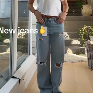 Zara jeans  - Säljer ett par slutsålda ljusblåa jeans med raka ben och flera slitningar på låren och knäna. Jeansen har hög midja och klassisk femficksdesign. Perfekta för en avslappnad och trendig look.