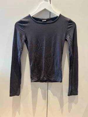 Mörkgrå långärmad topp - En stilren mörkgrå långärmad topp från Gina Tricot. Toppen har en rund halsringning och är figurnära i modellen. Perfekt att matcha med jeans eller kjol för en enkel och snygg look.