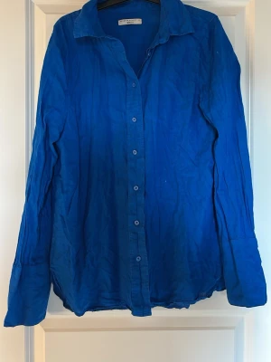 Blå linneskjorta från Gina Tricot - Snygg blå skjorta från Gina Tricot i luftig linnemix. Klassisk krage, knäppning framtill och långa ärmar. Perfekt för en avslappnad och trendig look.