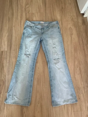 Ljusblå bootcut jeans med slitningar - Säljer ett par ljusblå bootcut jeans med snygga slitningar på framsidan. Jeansen har klassisk femficksdesign och låg midja. Perfekta för en avslappnad och trendig look. Materialet är denim i bomull.