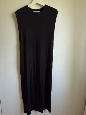 Svart långklänning från Amisu - En stilren svart långklänning från Amisu med ärmlös design och rund halsringning. Klänningen har en rak och enkel siluett, perfekt för dig som gillar minimalistisk stil. .