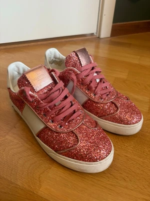 Glittriga rosa sneakers från Valentino - Säljer ett par riktigt snygga sneakers från Valentino med rosa glitter över hela skon, vita detaljer på sidorna och matchande rosa skosnören. Märkeslogga på plösen i metallic och vit sula. Perfekta för dig som vill sticka ut med din stil. Extra skosnören tillkommer. Bara använda två gånger! 