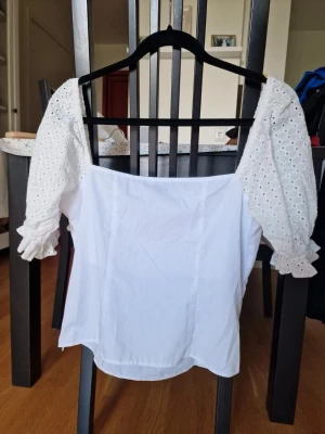 Vit topp med puffärmar och spetsdetaljer - Superfin vit topp från Asos med fyrkantig urringning och puffiga trekvartsärmar i broderad spets. Ärmarna har volangkant vid avslut och toppen är i ett lätt bomullstyg. Perfekt för en fräsch och trendig look. Storlek 42. Perfekt skick