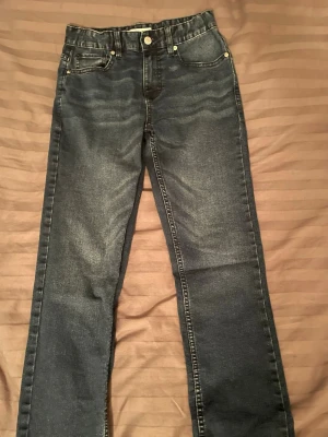 Mörkblå jeans från Calvin Klein - Snygga mörkblå jeans från Calvin Klein Jeans med klassisk femficksdesign och raka ben. Jeansen har subtila slitningar framtill och bakfickor med diskreta sömmar. Perfekta för en stilren och avslappnad look.