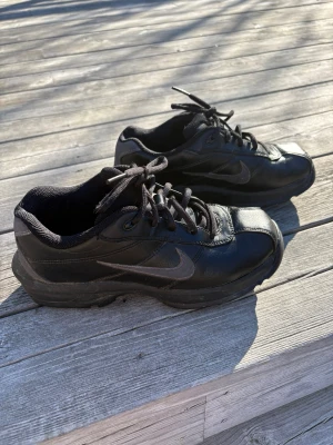 Svarta golfskor från Nike strl 36 - Säljer ett par svarta golfskor från Nike med klassisk swoosh-logga på sidan. Skorna har snörning, låg profil och slitstark gummisula. Perfekta för härliga  golfrundor. Storlek 36 (EU), 4Y (US).