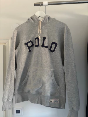 Ralph Lauren Hoodie/Grå - Snygg grå hoodie från Polo Ralph Lauren med stor POLO-text i mörkblått på bröstet. Hoodien är i använt skick. Hör av dig vid frågor eller funderingar!