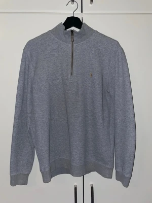 Grå halvzip tröja från Polo Ralph Lauren - Snygg grå långärmad tröja från Polo Ralph Lauren med halv dragkedja och liten broderad logga på bröstet. 