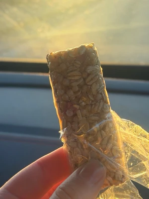 Krispig müslibar med frön - En rektangulär müslibar med solrosfrön och puffat ris, inslagen i genomskinlig plast. Färgen är gyllenbrun och baren ser ut att vara sötad, perfekt som snabb energi. Inget synligt märke på förpackningen.