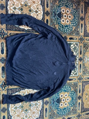 Svart halvzip tröja från Chaps - Snygg svart tröja från Chaps med halvzip och diskret logga på bröstet. Tillverkad i en mjuk bomulls- och kashmirblandning som känns riktigt skön mot huden. Perfekt till jeans eller chinos för en clean look.