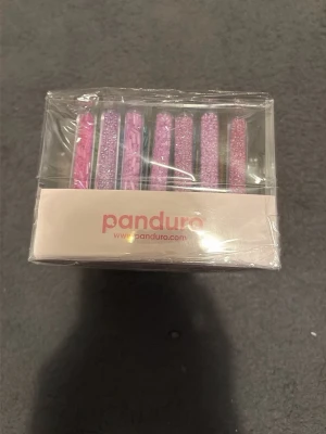 Panduro glitter pärlor i olika färger - Ett set med glitterpärlor från Panduro i flera olika färger, perfekt för pyssel och dekoration. Pärlorna kommer i en genomskinlig plastförpackning och har glittrande nyanser av rosa, lila, grönt, blått och gult.