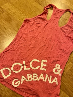 Korall linne: Dolce & Gabbana - Snyggt rosa korall linne med stort vitt tryck framtill på Dolce & Gabbana på baksidan💗 Modellen är ärmlös, tillverkad i mjukt bomullstyg. Perfekt inför sommaren ☀️