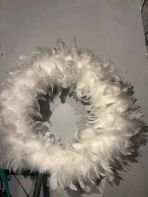 Vit krans med fjädrar - Säljer en rund krans täckt av fluffiga vita fjädrar. Perfekt som dekoration till dörren eller väggen för att skapa en mysig och stilren känsla. Kransen har en ögla för enkel upphängning och ger ett mjukt och elegant intryck.