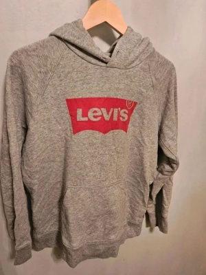Grå Levi's hoodie med röd logga - Levis hoodie M  Säljer en Levis hoodie som saknar snöret i luvan plus att den är lite missfärgad nere vid ena mudden på armen se bild  Kan även hämtas I Partille  E1