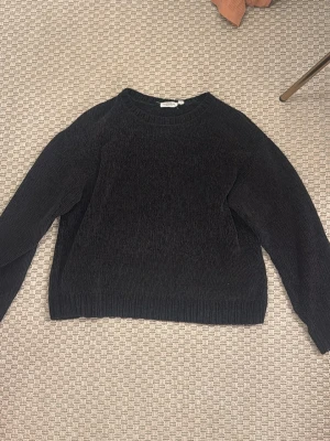 Svart stickad tröja - Mysig svart stickad tröja med rund halsringning och långa ärmar. Tröjan har en enkel, rak passform och ribbade muddar vid ärmslut och nederkant. Perfekt att styla med jeans eller kjol för en clean look.