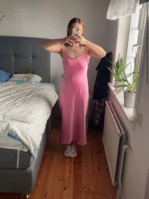 Rosa långklänning med smala axelband - Säljer en söt rosa långklänning med smala axelband och figurnära passform. Klänningen har en enkel och stilren design, perfekt för dig som gillar en feminin look. Materialet har en lätt glans och känns mjukt mot huden.
