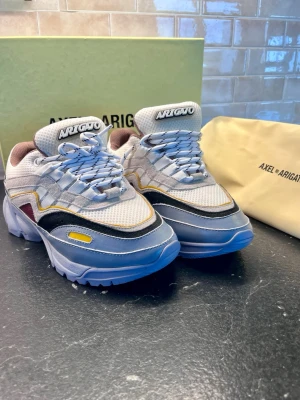 Axel Arigato multicolor sneakers - Snygga sneakers från Axel Arigato med chunky sula och coola färgblock i lila, vitt, svart, gult och vinrött. Mesh och mocka-material ger en modern vibe, och detaljer som broderad logga på tungan och kontrasterande paneler gör dem riktigt unika.