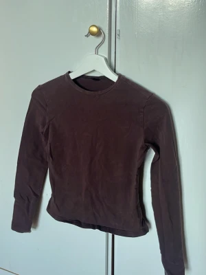 Brun långärmad topp i bomull - Mörkbrun långärmad topp med rund halsringning. Enkel och stilren design, tillverkad i mjuk bomull som sitter skönt mot kroppen. Perfekt att matcha med jeans eller kjol för en clean look.